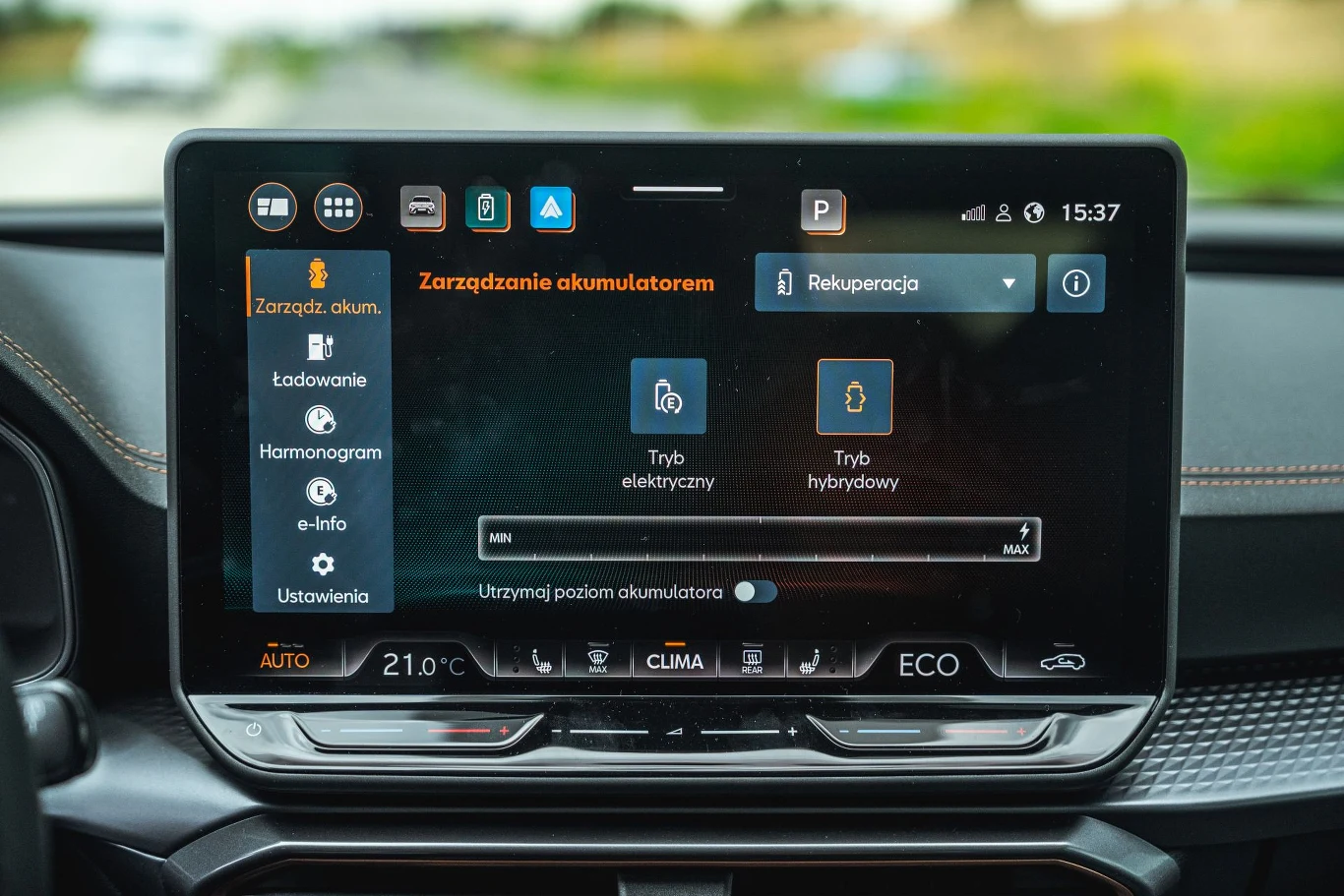 Hybryda plug-in Cupry Leon po rozładowaniu akumulatora cały czas pozostawia sobie rezerwę, by działać, jak klasyczna hybryda. Kolorowy ekran komputera pokładowego samochodu prezentujący opcje zarządzania akumulatorem i wybór trybów jazdy, przycisk klimatyzacji oraz skróty do nawigacji i multimediów na konsoli środkowej pojazdu.