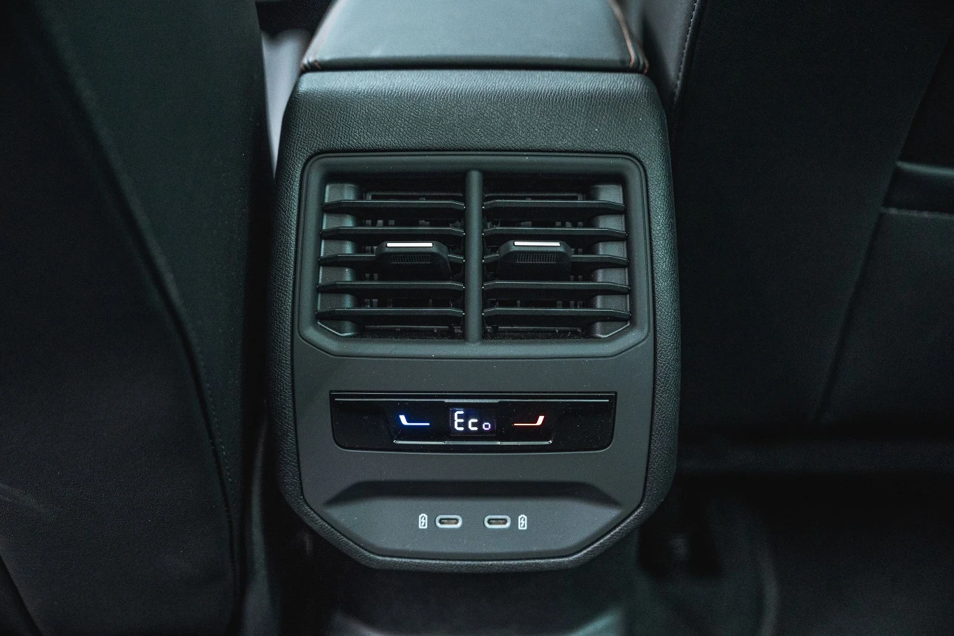 Już w standardowej wersji wyposażenia Cupra Leon jest wyposażona w trzystrefową klimatyzację automatyczną. Panel tylnej klimatyzacji samochodu z widocznymi kratkami wentylacyjnymi oraz cyfrowym wskaźnikiem trybu Eco i regulacją temperatury, otoczony czarnym wnętrzem pojazdu.