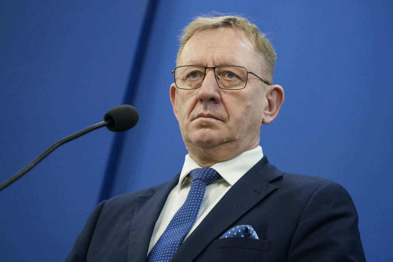 Poseł PiS Robert Telus udzielił zaskakującej odpowiedzi na pytanie o bitcoina Mężczyzna w garniturze i okularach stoi przed mikrofonem na tle niebieskiej ściany, twarz ma poważny wyraz, całość sugeruje udział w oficjalnym wydarzeniu lub konferencji prasowej.