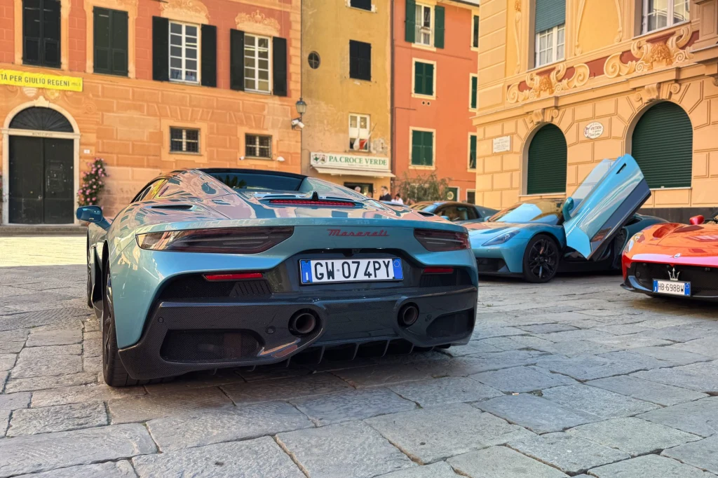 Maserati MCPura Cielo w sercu Sestri Levante. Ten samochód wygląda tu jak część miejskiej architektury Luksusowe, sportowe samochody Maserati zaparkowane na brukowanym placu w otoczeniu kolorowych, włoskich kamienic, jeden z samochodów ma uniesione drzwi typu motyla.