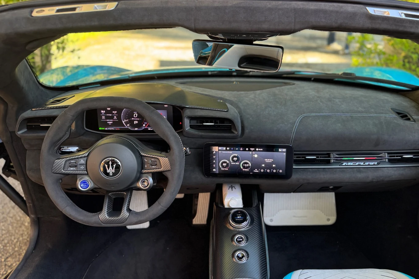 Luksusowe wnętrze sportowego samochodu Maserati wyposażone w zaawansowaną kierownicę, cyfrowy wyświetlacz i duży ekran dotykowy na środkowej konsoli, obszycia z wysokiej jakości materiałów, jasne pedały i eleganckie detale.