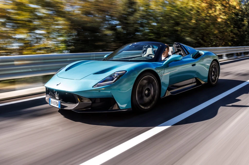 3.0 V6 Nettuno, 630 KM, napęd na tył. MCPura Cielo nie tylko brzmi jak supersamochód – on naprawdę nim jest Sportowy samochód Maserati MC20 z otwartym dachem sunie szybko po asfaltowej drodze, otoczony rozmytym tłem drzew, podkreślającym prędkość i dynamiczny charakter auta.