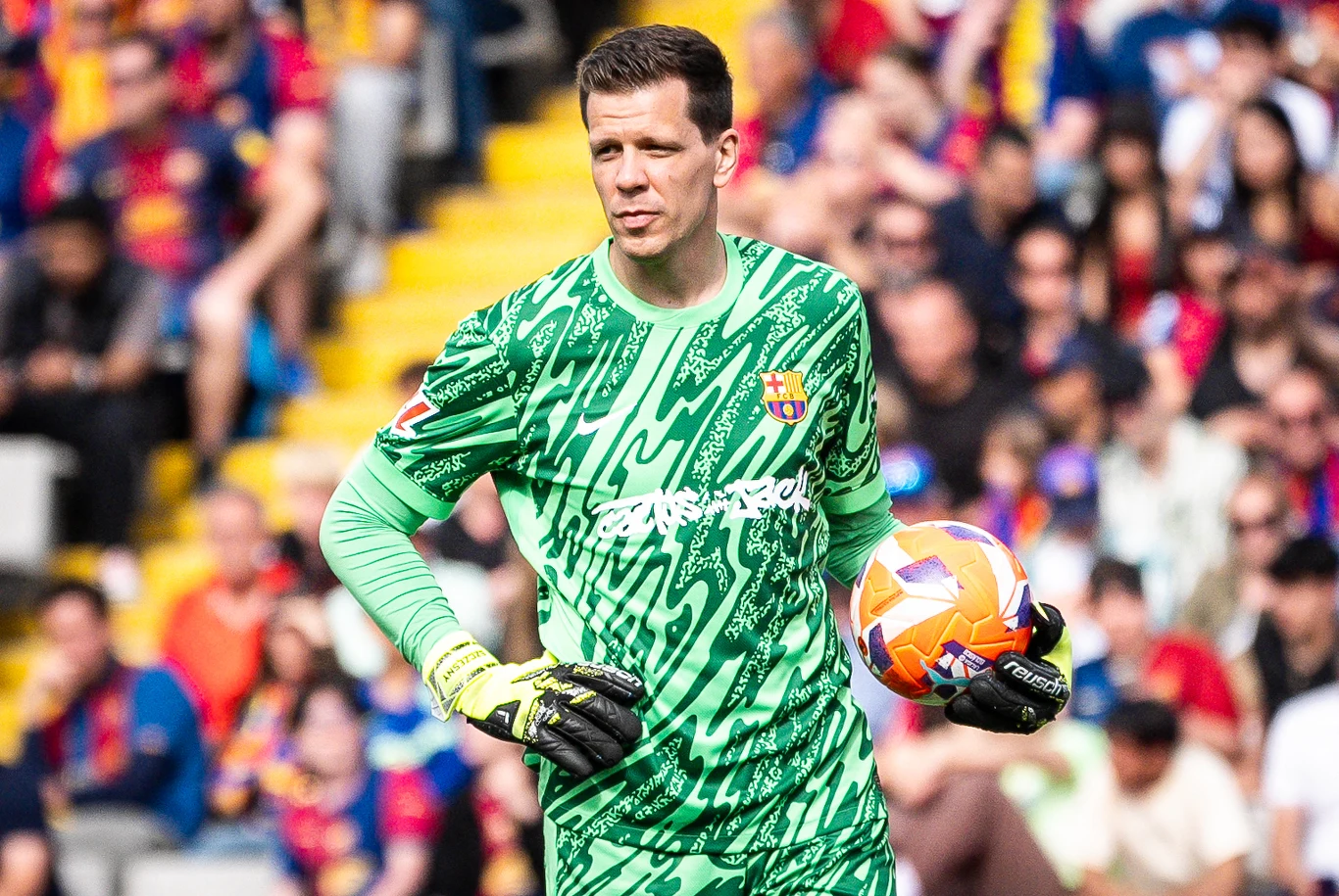 Wojciech Szczęsny Bramkarz w zielonym stroju piłkarskim z piłką w ręce stoi na boisku podczas meczu, w tle liczna publiczność na trybunach.