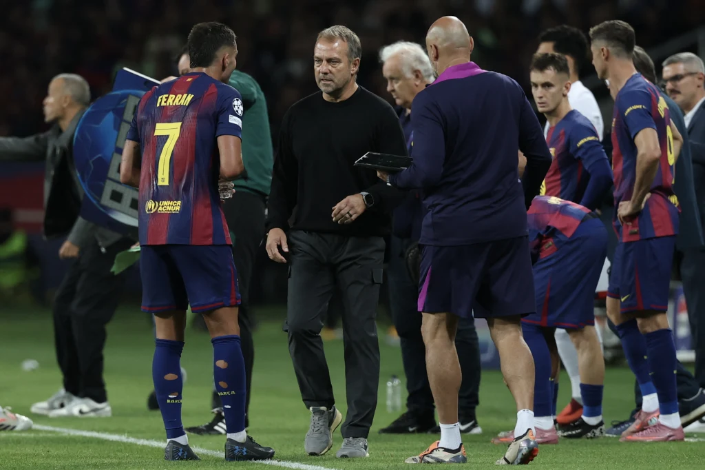 Hansi Flick z zawodnikami FC Barcelony Zawodnik piłkarskiej drużyny w stroju meczowym rozmawia z trenerem przy linii bocznej boiska, w tle pozostali członkowie sztabu i zawodnicy szykujący się do zmiany