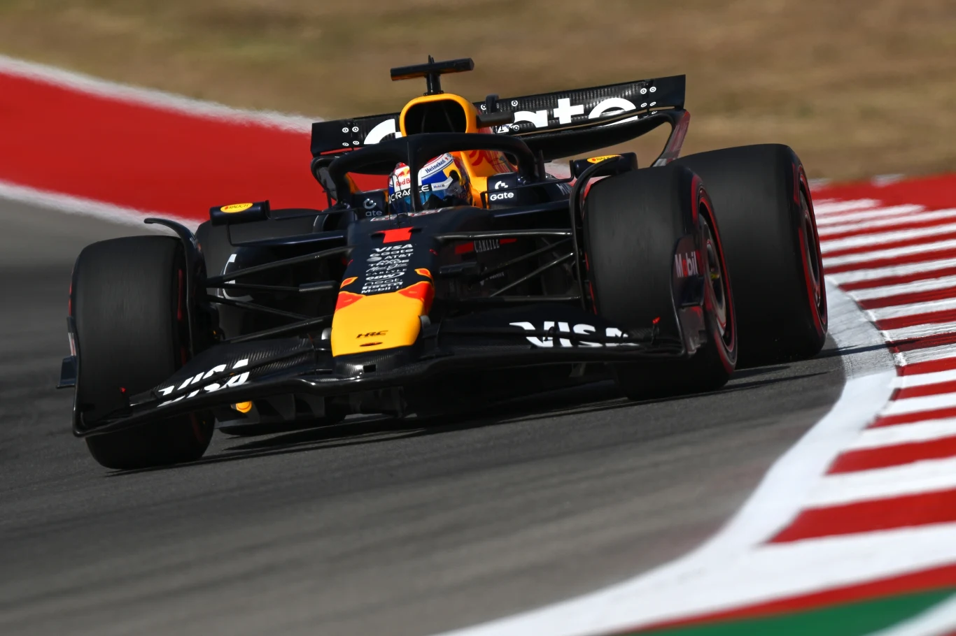 Max Verstappen Samochód wyścigowy Formuły 1 na torze, z wyraźnie widocznymi sponsorami oraz charakterystycznymi malowaniami zespołu, pokonujący zakręt na asfaltowym torze otoczonym pasem czerwono-białych krawężników.