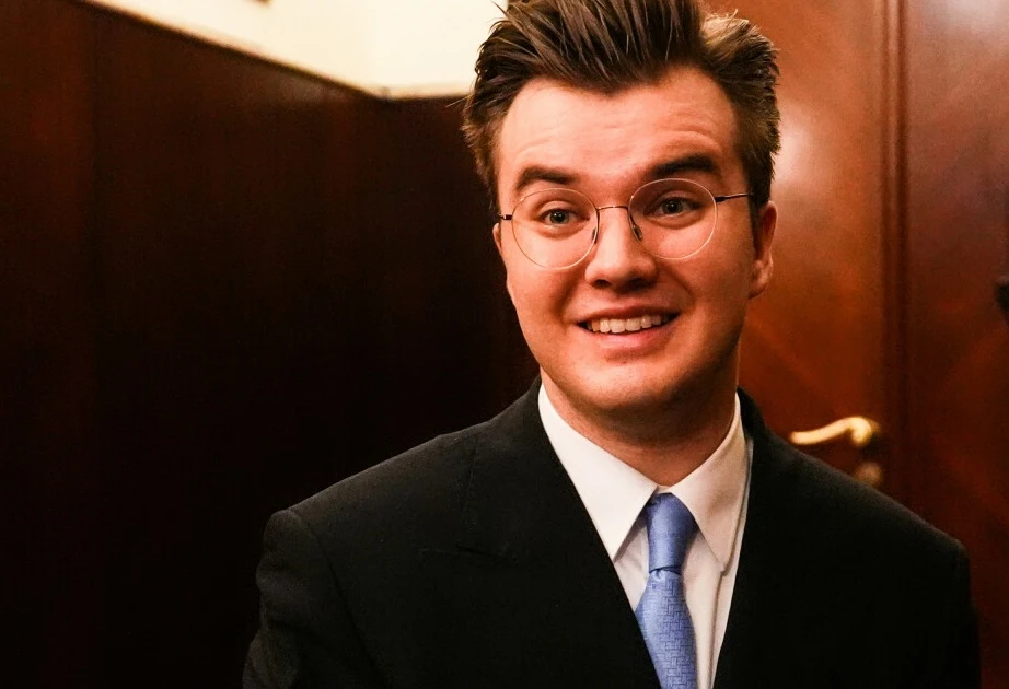 Piotr Alexewicz zagrał finałowy koncert w niedzielę 19 października Uśmiechnięty młody mężczyzna w garniturze i okularach, stojący w eleganckim pomieszczeniu z drewnianymi panelami.