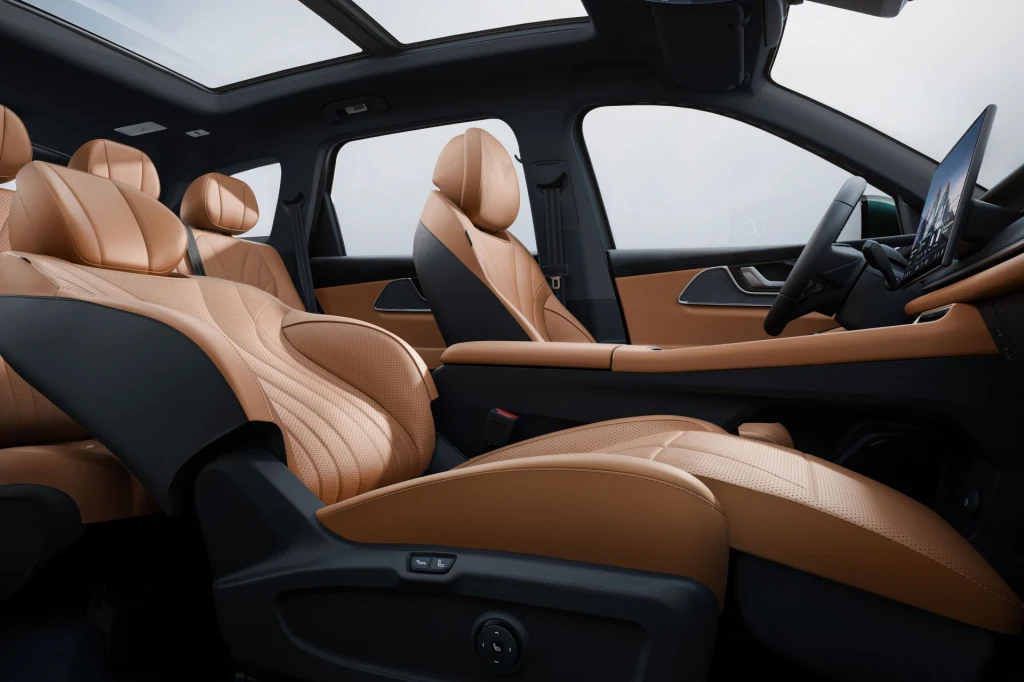 Fotel pasażera z przodu wyposażony jest w elektrycznie wysuwany podnóżek. Luksusowe wnętrze samochodu wyposażone w skórzane fotele w kolorze jasnego brązu, panoramiczny dach oraz nowoczesną deskę rozdzielczą z dużym ekranem dotykowym.