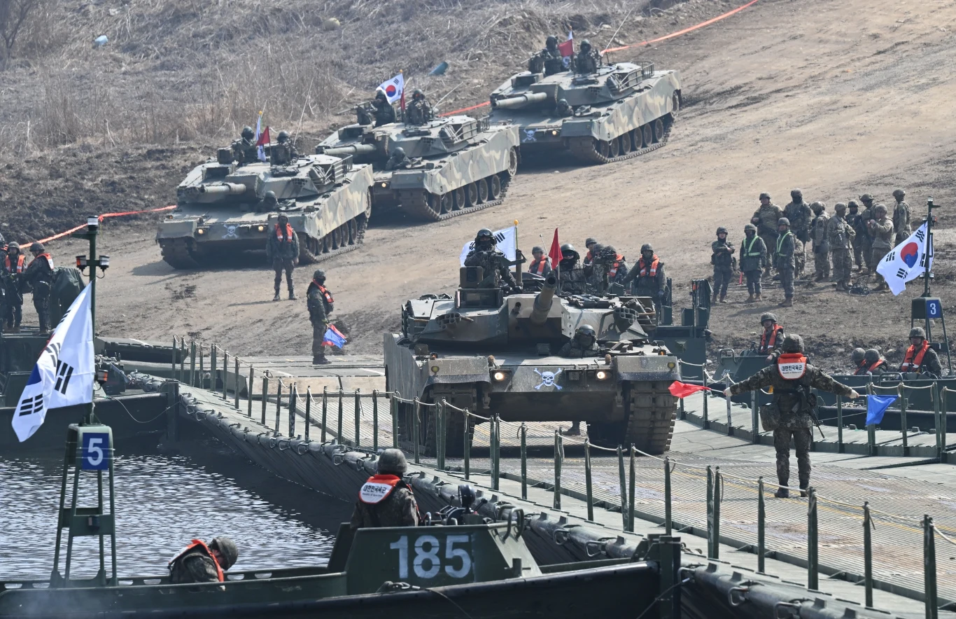 Korea Południowa zamierza stać się czwartym największym mocarstwem obronnym Czołgi południowokoreańskiej armii przejeżdżają przez kładkę pontonową, wokół zgromadzeni żołnierze oraz flagi Korei Południowej w otoczeniu wojskowej infrastruktury i pagórkowatego terenu.