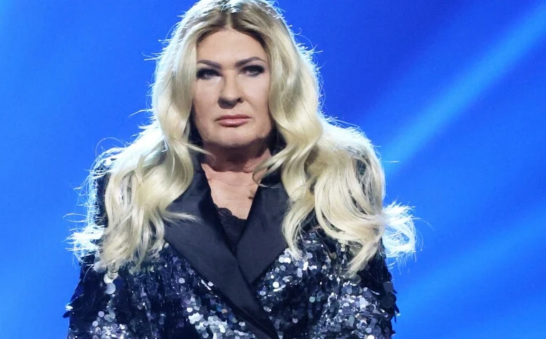 Beata Kozidrak zdradziła swój sposób na anonimowość Kobieta z długimi blond włosami w błyszczącej marynarce na tle niebieskiego światła scenicznego, z wyrazistym makijażem i poważnym wyrazem twarzy.