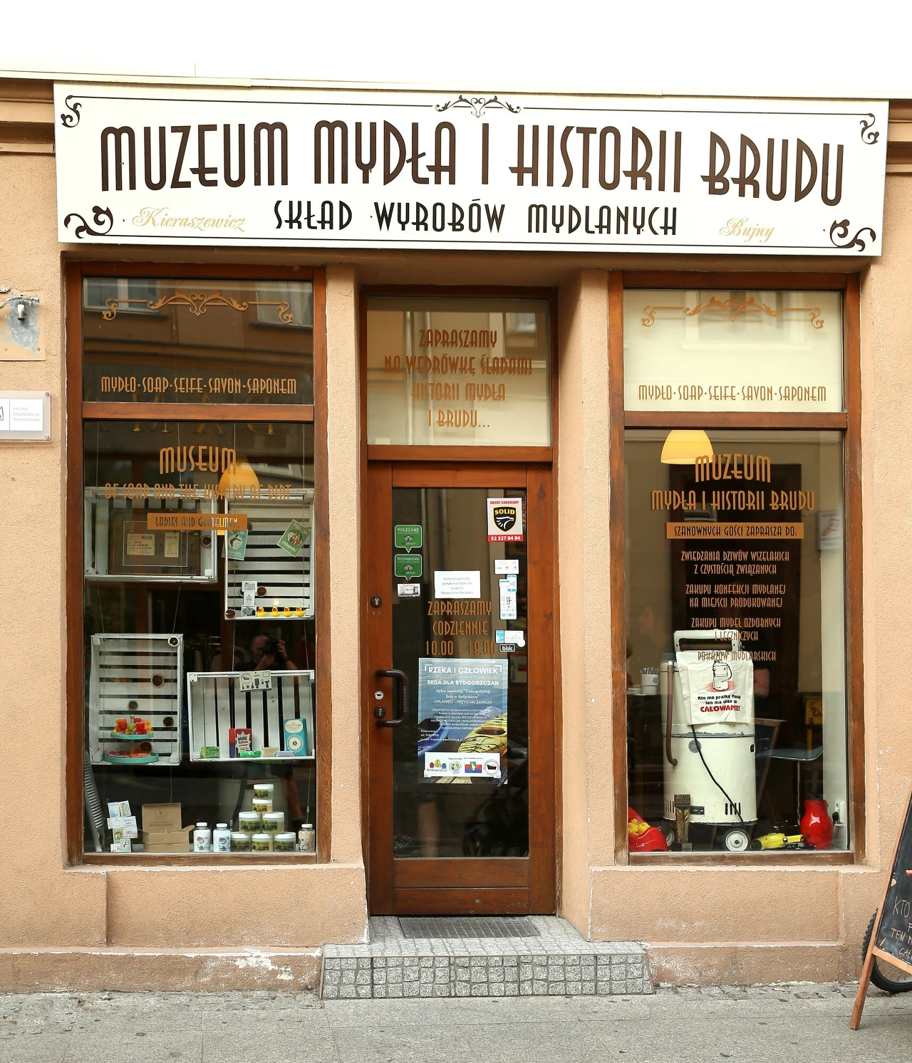 Muzeum Mydła i Historii Brudu w Bydgoszczy Fasada muzeum z dużymi oknami wystawowymi prezentującymi eksponaty oraz wejście do środka, nad drzwiami widoczny szyld z nazwą Muzeum Mydła i Historii Brudu.