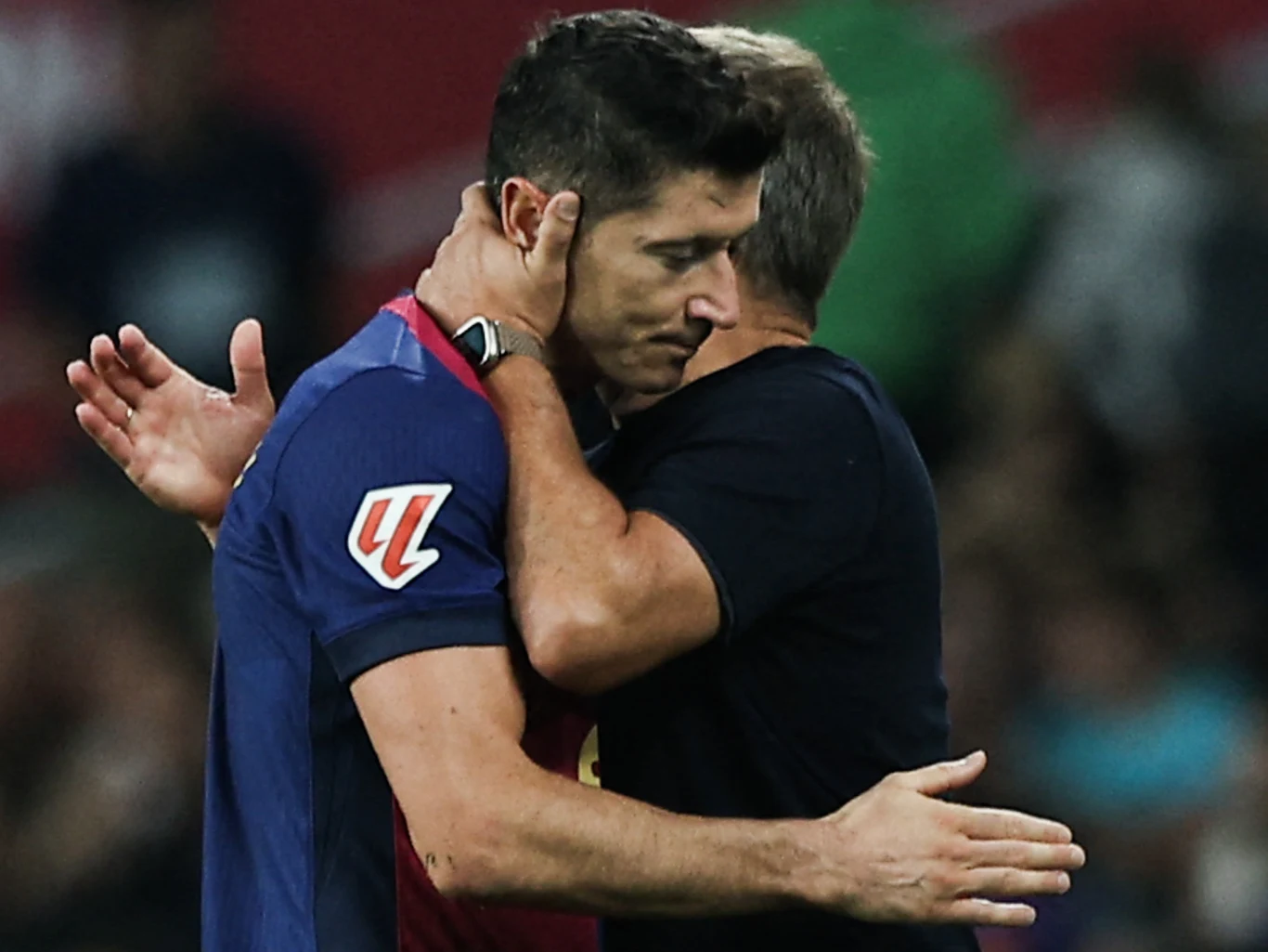 Robert Lewandowski i Hansi Flick Dwóch mężczyzn obejmujących się na tle stadionu, jeden ubrany w sportową koszulkę, drugi w czarną koszulkę, atmosfera wyraża wsparcie i emocje po wydarzeniu sportowym.