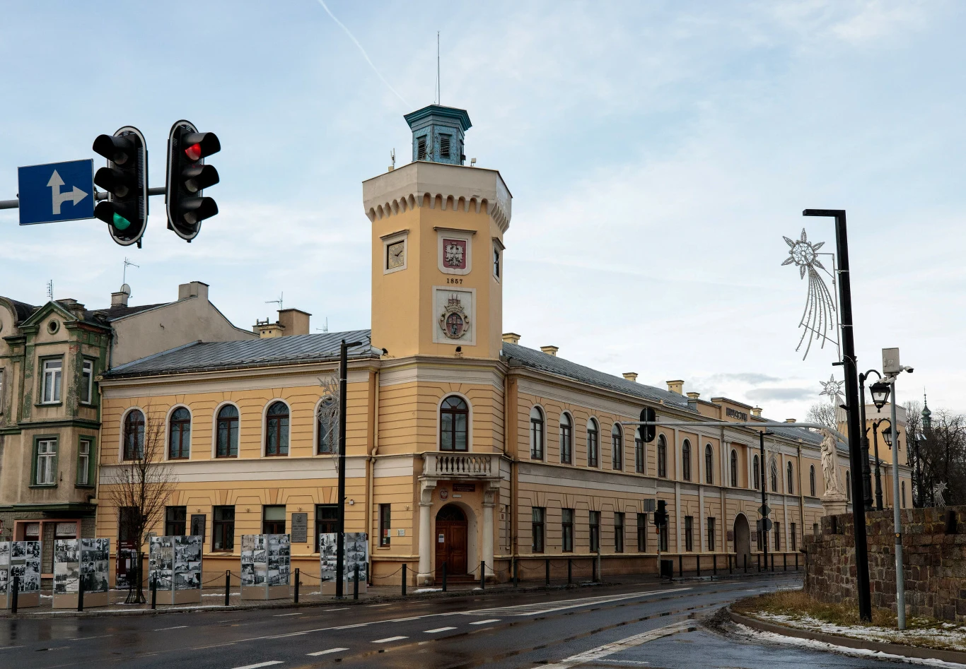 Radomsko zajęło drugie miejsce w raporcie Alarmu Smogowego 2024 Historyczny budynek ratusza z wieżą zegarową, utrzymany w jasnych kolorach, położony przy głównej ulicy, z widocznymi lampami miejskimi i sygnalizacją świetlną, w tle ozdoba świąteczna w kształcie gwiazdy.