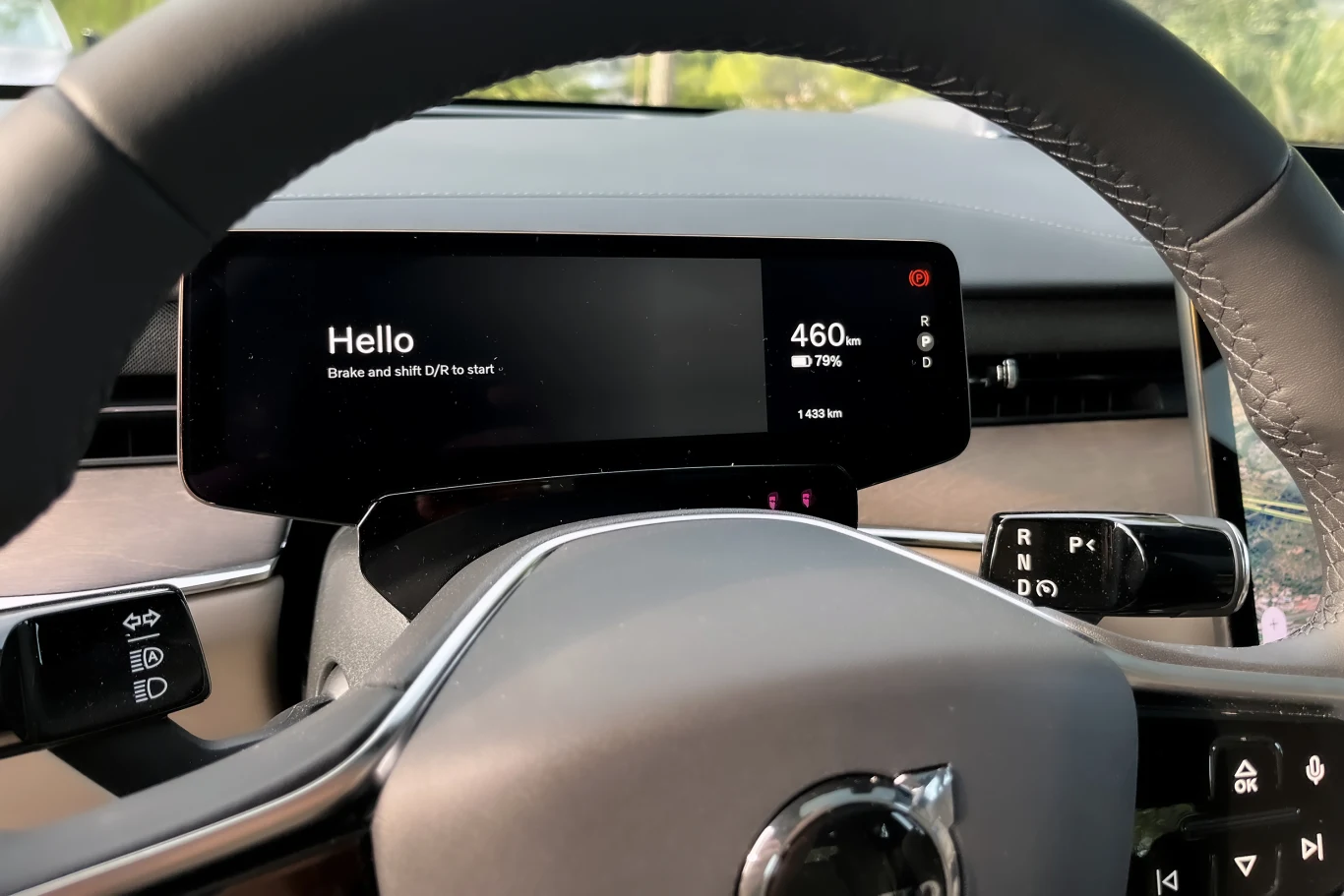 Cyfrowy wyświetlacz za kierownicą nowoczesnego samochodu z widocznym napisem powitalnym i informacjami o zasięgu oraz stanie baterii, otoczony eleganckim wnętrzem pojazdu i wielofunkcyjną kierownicą.