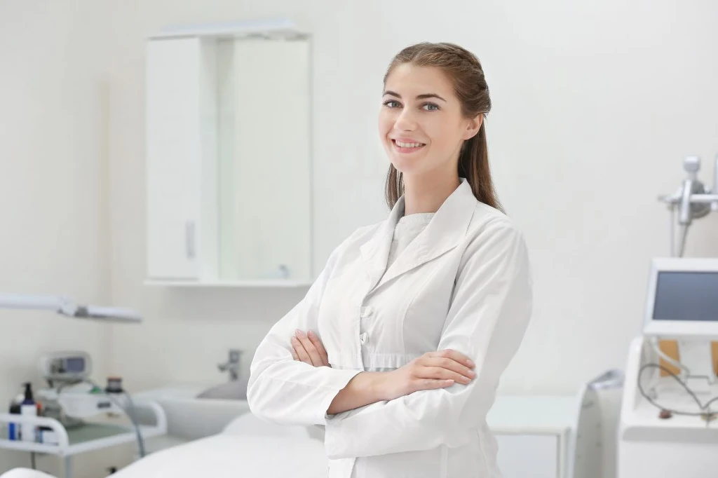 Dermatolodzy są zafascynowani nowym składnikiem anti-age Uśmiechnięta kobieta w białym fartuchu z założonymi rękami stoi w jasnym, nowoczesnym gabinecie medycznym