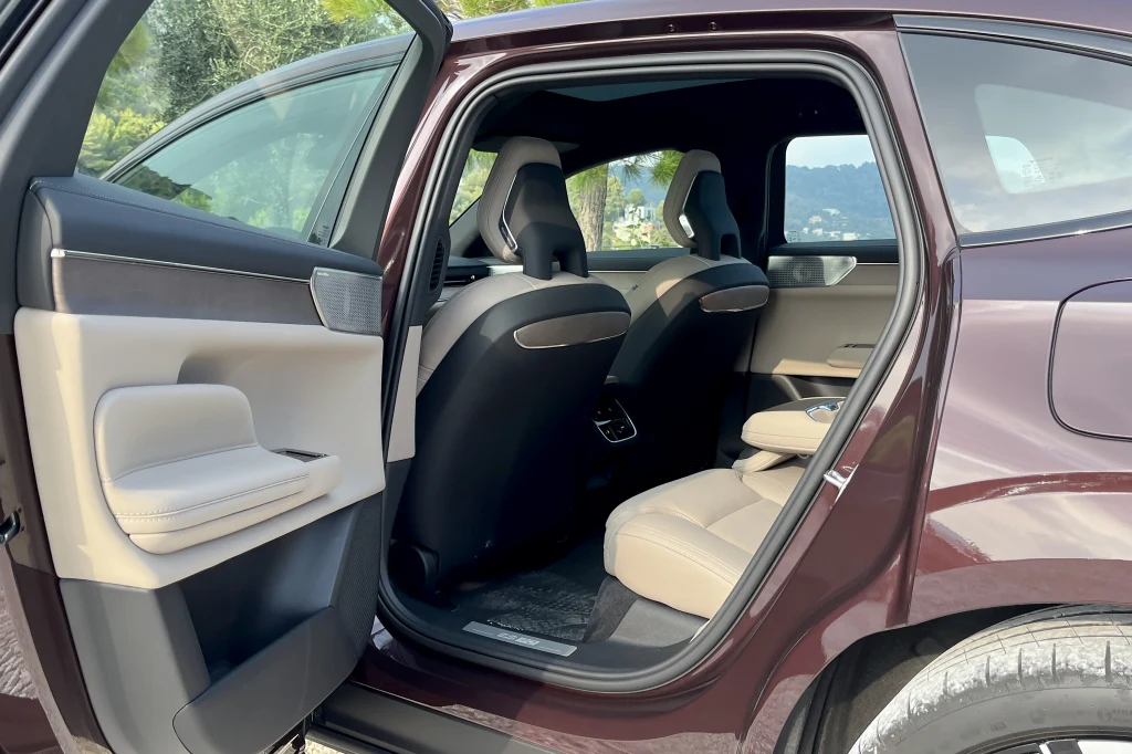 Otwarta tylna część samochodu z widocznym wnętrzem w jasnej kolorystyce, dwoma fotelami przednimi, przestronną kanapą tylną i fragmentem drzwi oraz elementami wykończenia auta klasy premium.