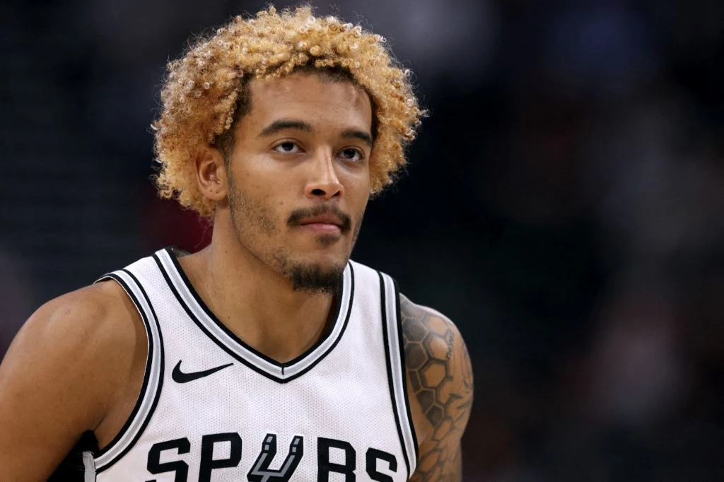 Jeremy Sochan nie przedłużył umowy z San Antonio Spurs Koszykarz w białej koszulce drużyny Spurs z wyraźnymi tatuażami na ramieniu oraz charakterystycznymi kręconymi, blond włosami stoi na boisku w trakcie meczu.