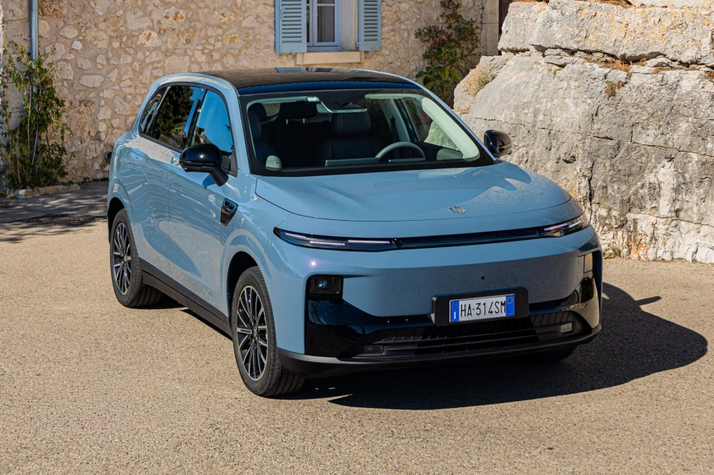 Jasnoniebieski samochód elektryczny SUV zaparkowany na tle kamiennych ścian i okna, z włoską tablicą rejestracyjną, prezentujący nowoczesny design i eleganckie wykończenie.