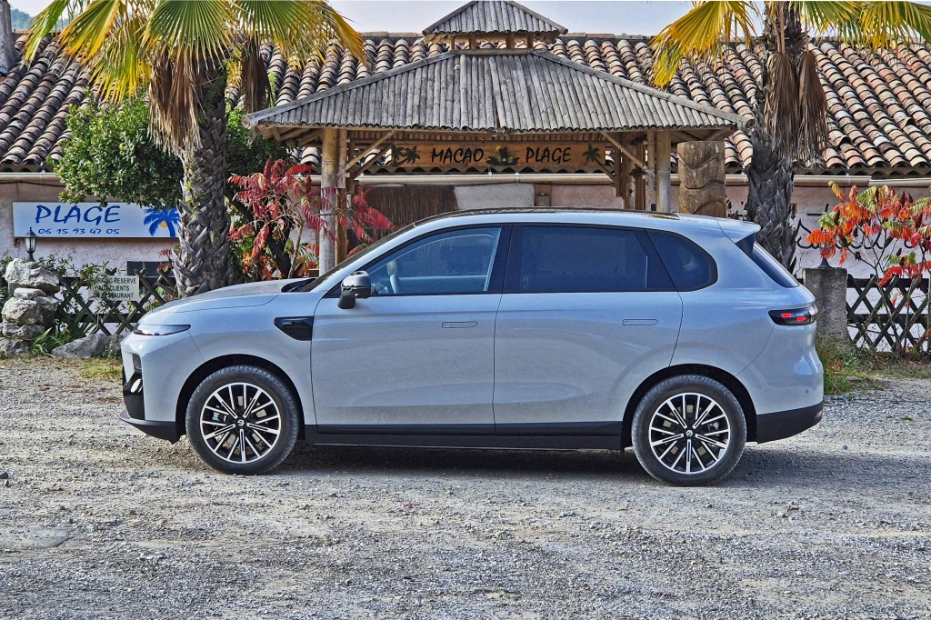 Leapmotor B10 mierzy nieco ponad 4,5 m, a jego rozstaw osi to 2,74 m Srebrny SUV zaparkowany na żwirowym placu, w tle egzotyczny budynek z dachem pokrytym dachówką, otoczony palmami i ozdobnymi roślinami.