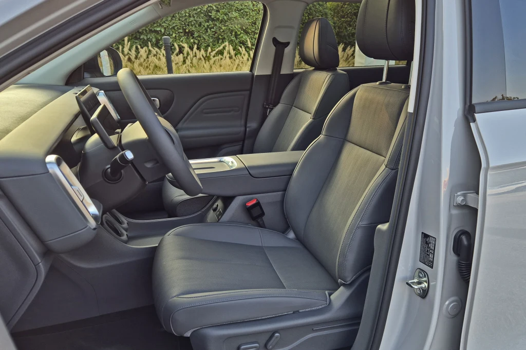 Fotele w B10 są wygodne, ale mają przeciętne trzymanie boczne Widok na przednie wnętrze nowoczesnego samochodu z otwartymi drzwiami, dwa wygodne fotele pokryte skórzaną tapicerką, czytelna deska rozdzielcza z ekranem dotykowym, przestronna przestrzeń, starannie wykończone detale.