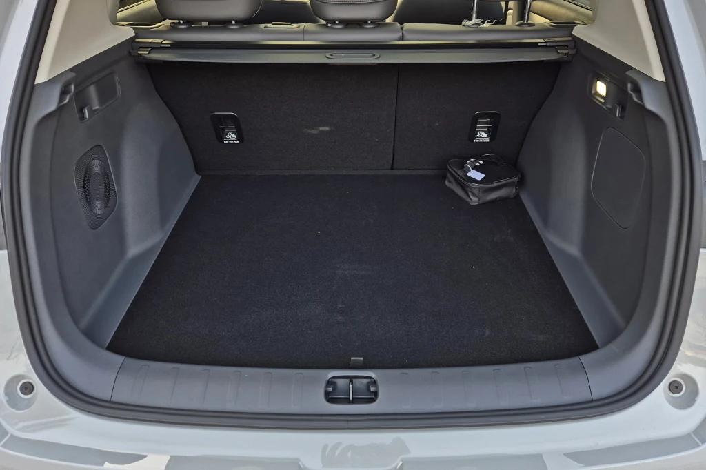 Bagażnik Leapmotora B10 na żywo wydaje się nieco wąski, ale ma niezłą pojemność i ma bardzo regularne kształty Pusty bagażnik samochodu z czarną tapicerką, w rogu widoczne niewielkie czarne etui lub zestaw narzędzi, oświetlenie po prawej stronie, tylne siedzenia samochodu w tle.