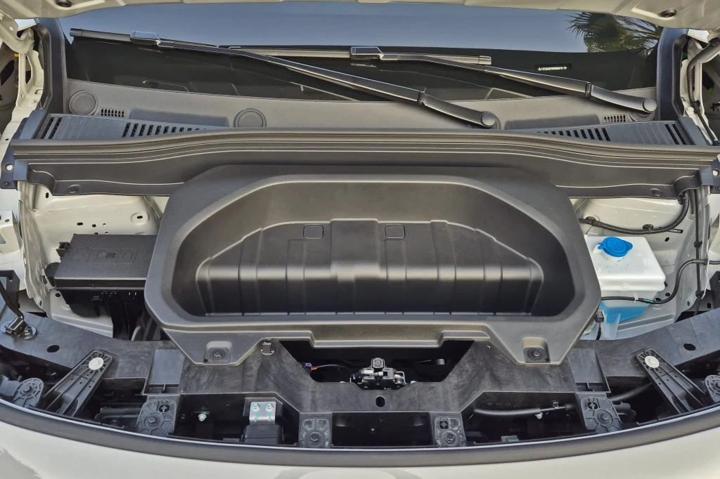 Pod maską B10 znajdziemy niewielki schowek, akumulator, zbiornik płynu do spryskiwaczy i sporo wolnej przestrzeni Otwarty przedni bagażnik samochodu elektrycznego z widocznym schowkiem oraz umieszczoną po prawej stronie niebieską nakrętką zbiornika na płyn.