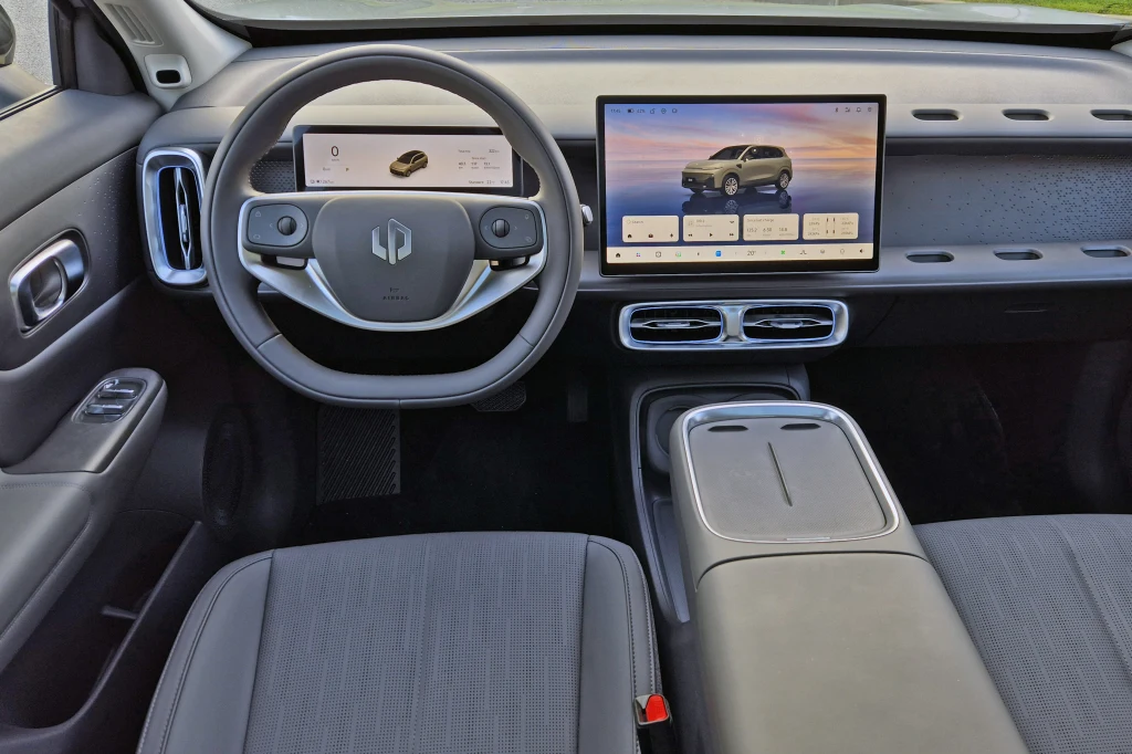 Chromowane nawiewy urozmaicają wnętrze Leapmotora B10, ale sama deska rozdzielcza to połacie plastiku Nowoczesna deska rozdzielcza samochodu elektrycznego z dużym dotykowym ekranem centralnym, zaawansowaną kierownicą oraz panelami sterowania na drzwiach kierowcy i konsoli środkowej.