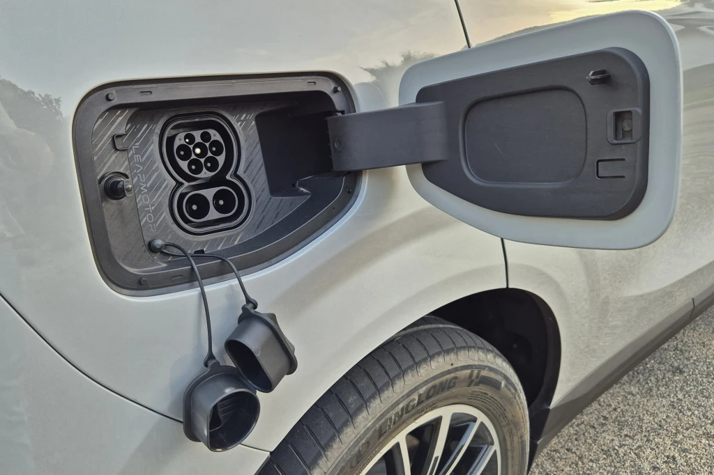 B10 z większą baterią pozwala na ładowanie z mocą 168 kW Otwarta klapka wlewu prądu samochodu elektrycznego z widocznym złączem ładowania oraz gumowymi osłonami przewodów, fragment tylnego nadkola z oponą.