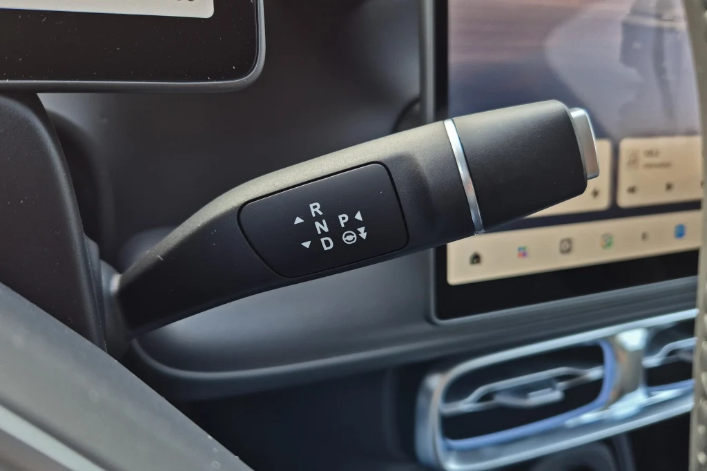 Leapmotor B10 to kolejny samochód, w którym wybierak kierunku jazdy jest wzorowany na rozwiązaniu stosowanym przez Mercedesa Dźwignia automatycznej skrzyni biegów z oznaczeniami trybów jazdy zamontowana przy kierownicy samochodu, w tle wyświetlacze cyfrowe kokpitu.