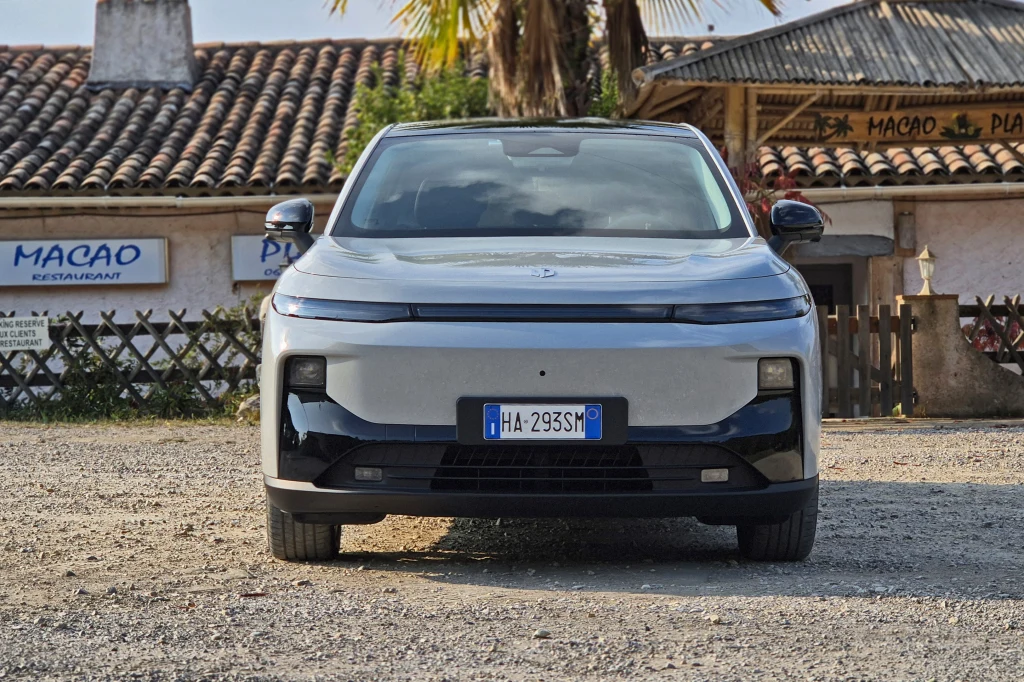 Światła do jazdy dziennej zlewają się z wąskim czarnym paskiem, zaś główne reflektory z lakierowanymi na czarno elementami zderzaka. Według projektantów, dopóki ich nie włączymy, w ogóle nie widać, że tam są Srebrny, nowoczesny samochód elektryczny zaparkowany na żwirowym placu na tle klimatycznej restauracji z czerwonym dachem i palmą. Na tablicy rejestracyjnej widoczny włoski numer.