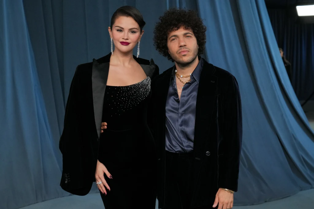Selena Gomez i Benny Bianco na gali Academy Museum 2025 Dwie elegancko ubrane osoby pozują razem na tle niebieskich kotar, kobieta w czarnej, ozdobionej cekinami sukni z marynarką, mężczyzna w ciemnym garniturze i koszuli, oboje patrzą w stronę obiektywu.