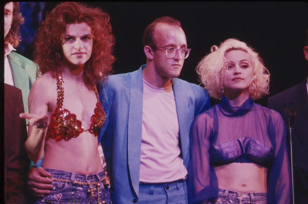 Po zyskaniu sławy Keith Hering przyjaźnił się z wieloma zamożnymi celebrytami, m.in. z Madonną Trzy osoby stoją obok siebie na scenie. Kobieta po lewej ma rude, kręcone włosy oraz kolorowy, brokatowy biustonosz, mężczyzna w środku nosi niebieski garnitur i okulary, a kobieta po prawej ma jasne, rozpuszczone włosy i fioletową, przezroczystą bluzk...