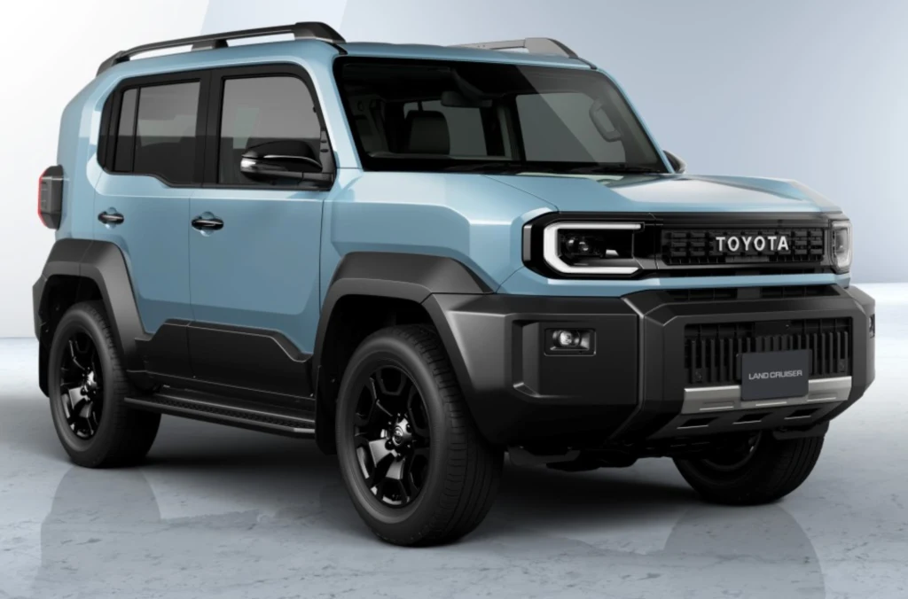 Choć Land Cruiser FJ jest mniejszy od serii 250 i 300, konstruktorzy nie zrezygnowali z jego terenowego DNA. Nowoczesny samochód terenowy Toyota Land Cruiser w kolorze niebieskim z czarnymi dodatkami, stojący na jasnym tle, widoczne wyraziste nadkola, masywna sylwetka oraz czarne felgi.