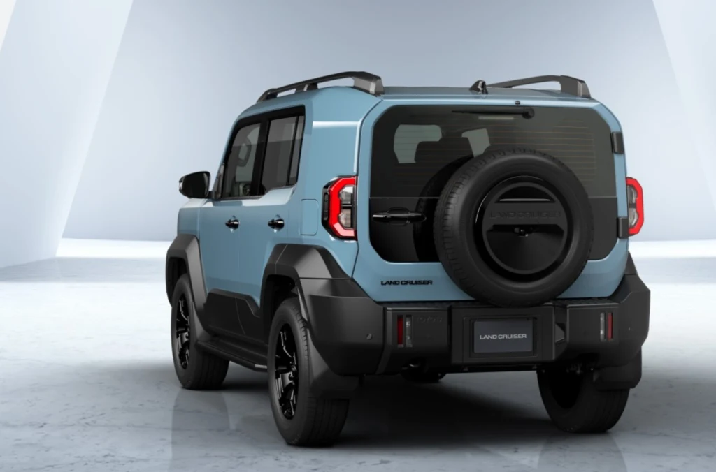 Kanciasta sylwetka, proste linie i szerokie błotniki podkreślają solidność konstrukcji. Niebieski samochód terenowy Toyota Land Cruiser z czarnym kołem zapasowym zamontowanym na tylnych drzwiach, nowoczesna stylistyka nadwozia, pojazd ustawiony na jasnym tle.