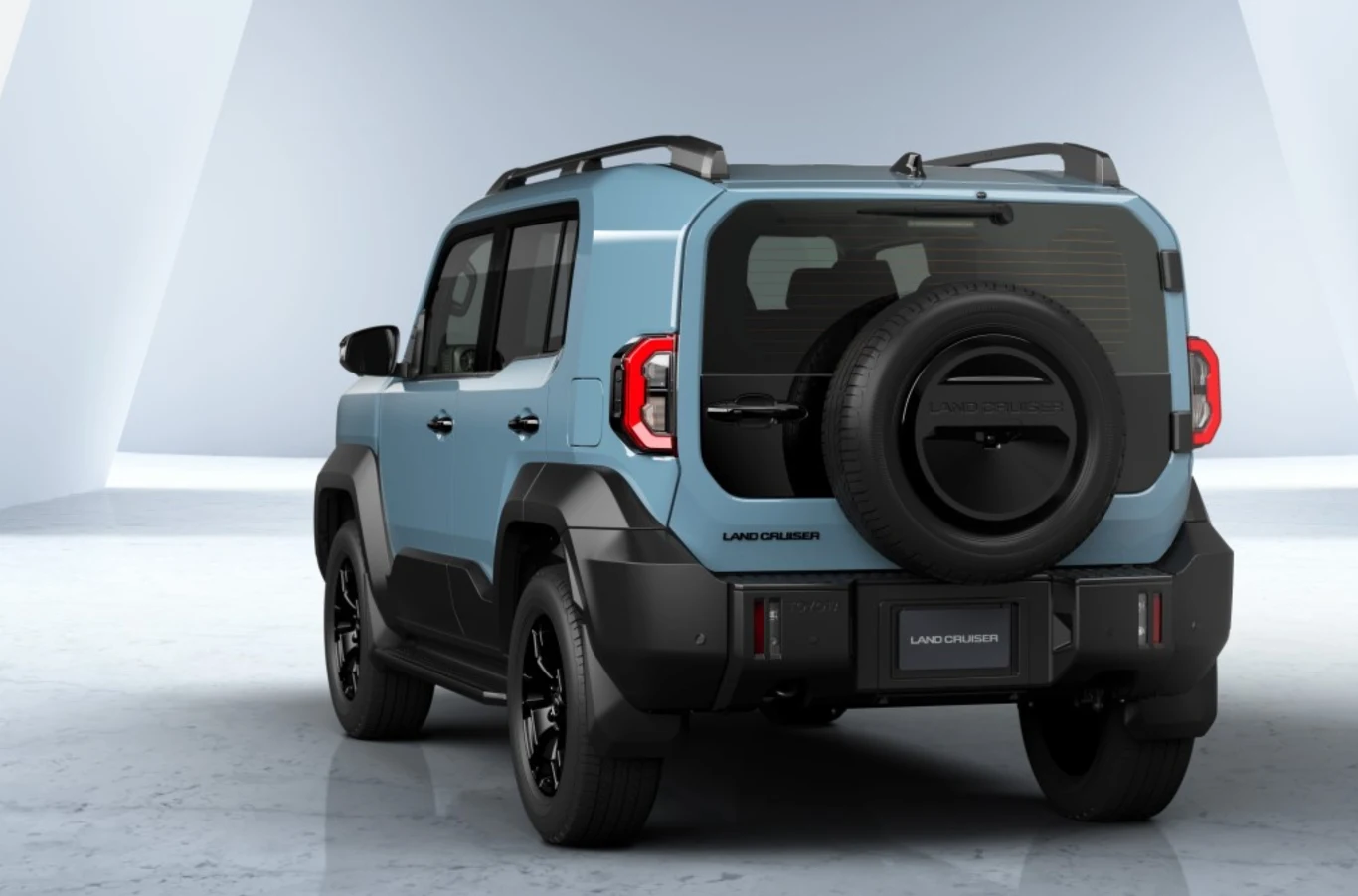 Niebieski samochód terenowy Toyota Land Cruiser z czarnym kołem zapasowym zamontowanym na tylnych drzwiach, nowoczesna stylistyka nadwozia, pojazd ustawiony na jasnym tle.