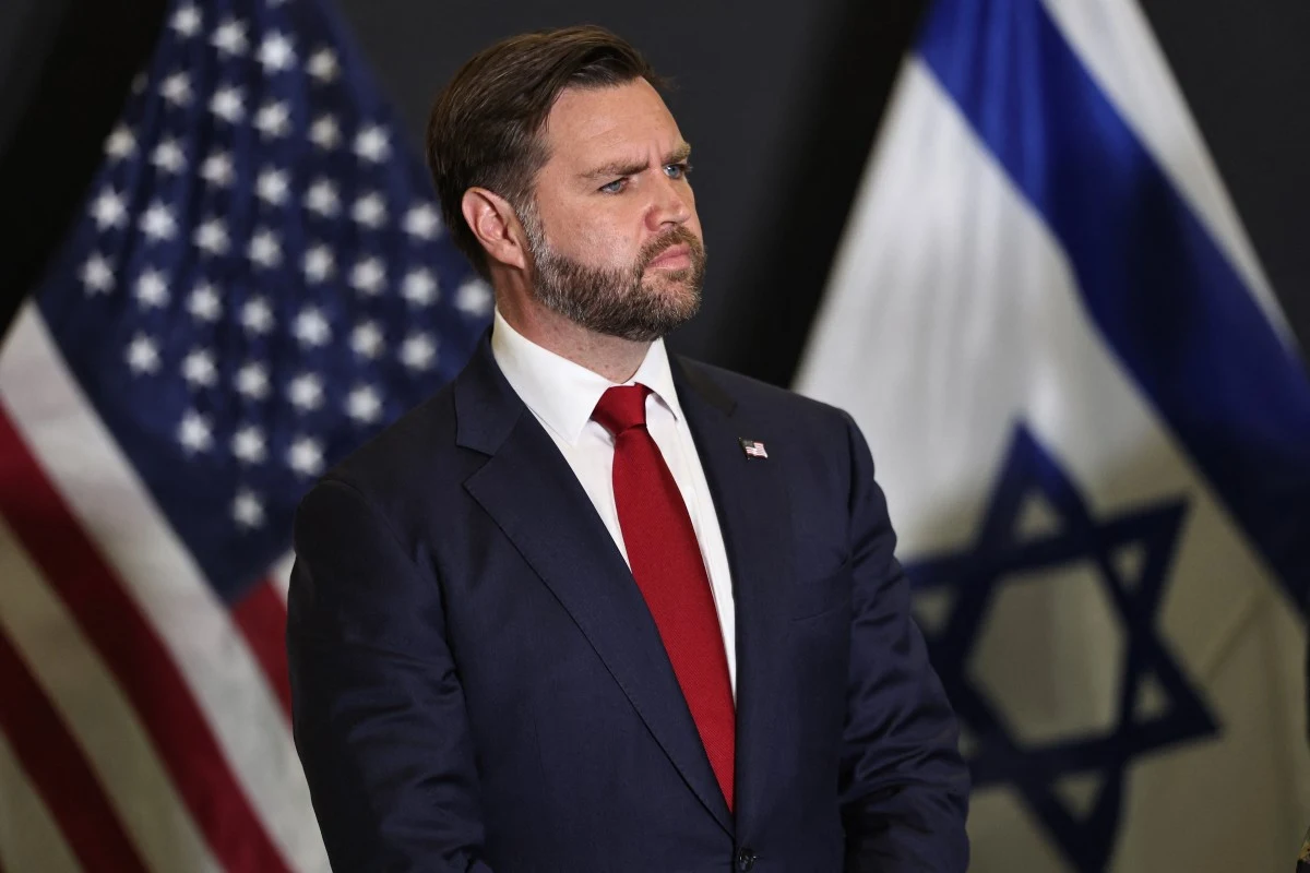 Wiceprezydent USA JD Vance Mężczyzna w garniturze z czerwoną krawatą stoi na tle flag Stanów Zjednoczonych i Izraela, przyjmuje poważną postawę, patrzy w bok.