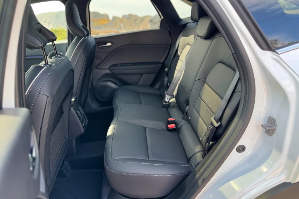 Czarne, skórzane tylne siedzenia samochodu z widocznymi pasami bezpieczeństwa, przestronne wnętrze z wyraźnie wyprofilowanymi oparciami, lekkie światło wpadające przez boczne okna.