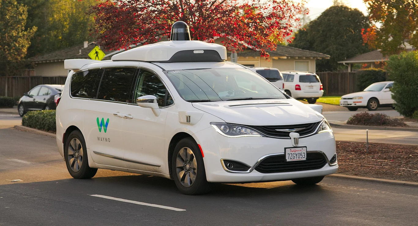 Waymo stale aktualizuje oprogramowanie swoich autonomicznych taksówek, ucząc ich także nowych tras i zachowań. Do tego wykorzystuje testowe modele na bazie Chrayslera Pacifica, które jeżdżą z kierowcą, mogącym zainterweniować w momencie błędu Biały samochód autonomiczny z logo Waymo wyposażony w czujniki i kamery poruszający się po ulicy w dzielnicy mieszkalnej podczas słonecznego dnia