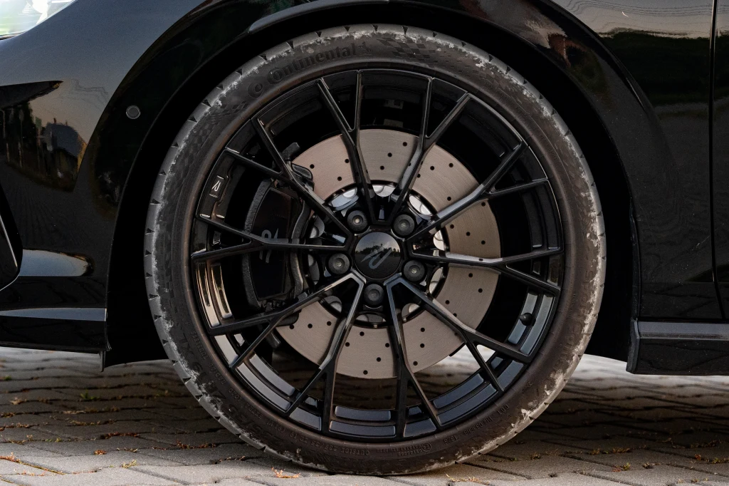 Volkswagen Golf R standardowo wyjeżdża z fabryki na 18-calowych felgach. W Black Edition seryjnie otrzymujemy czarne "dziewiętnastki" Czarna, wieloramienna felga z widocznymi nawierconymi tarczami hamulcowymi sportowego samochodu na tle brukowanej nawierzchni, ostro zaakcentowane detale metalowe i opona.