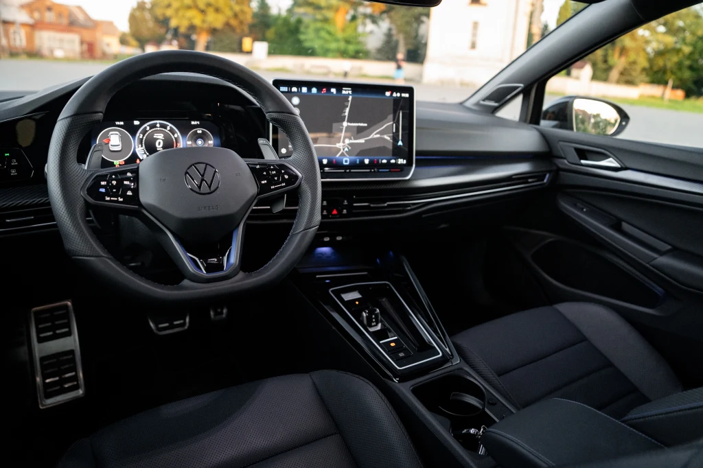 Volkswagen Golf R Black Edition Kokpit nowoczesnego samochodu marki Volkswagen z cyfrowymi licznikami, dużym ekranem dotykowym na konsoli środkowej, sportową kierownicą oraz eleganckim, czarnym wykończeniem wnętrza.