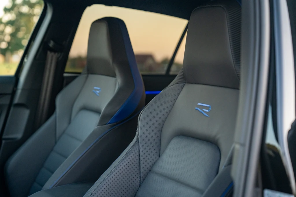 Volkswagen Golf R Black Edition Dwa nowoczesne sportowe fotele samochodowe z logo R na zagłówkach, tapicerowane ciemnym materiałem, otoczone subtelnym, niebieskim oświetleniem wnętrza auta.