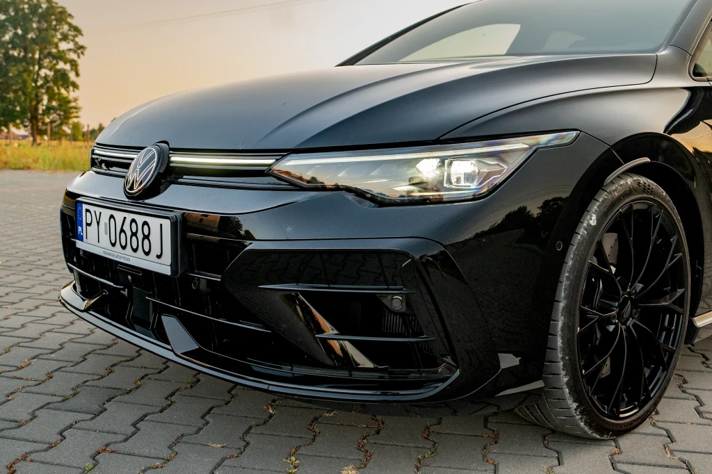 Volkswagen Golf R Black Edition Czarny samochód marki Volkswagen z charakterystycznym logo i nowoczesnym reflektorem, widoczna polska tablica rejestracyjna oraz czarne, sportowe felgi zaparkowane na kostce brukowej