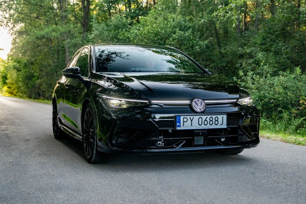 Volkswagen Golf R Black Edition Czarny samochód marki Volkswagen stoi na asfaltowej drodze otoczonej zielonym lasem, światło słoneczne przebija się przez drzewa w tle, tablica rejestracyjna z numerem PY 0688J widoczna na przodzie auta.