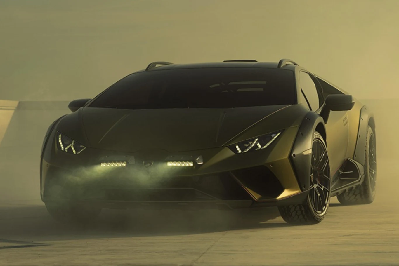 Tak prezentuje się Lamborghini Huracan Sterrato. Matowy, ciemnozielony sportowy samochód z agresywnymi liniami nadwozia stoi na otwartej przestrzeni, otoczony mgłą i delikatnym dymem unoszącym się przed maską, z wyrazistymi światłami LED i masywnymi felgami.