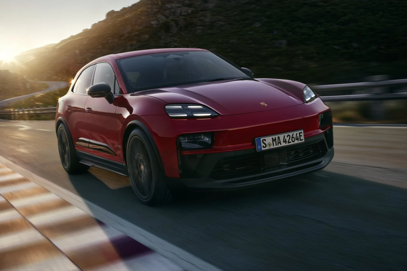 Porsche Macan GTS waży prawie 2,4 tony, ale "setkę" robi w 3,8 sekundy. Czerwony samochód marki Porsche jedzie dynamicznie po pustej, krętej drodze przy zachodzącym słońcu, na tle górskiego krajobrazu.