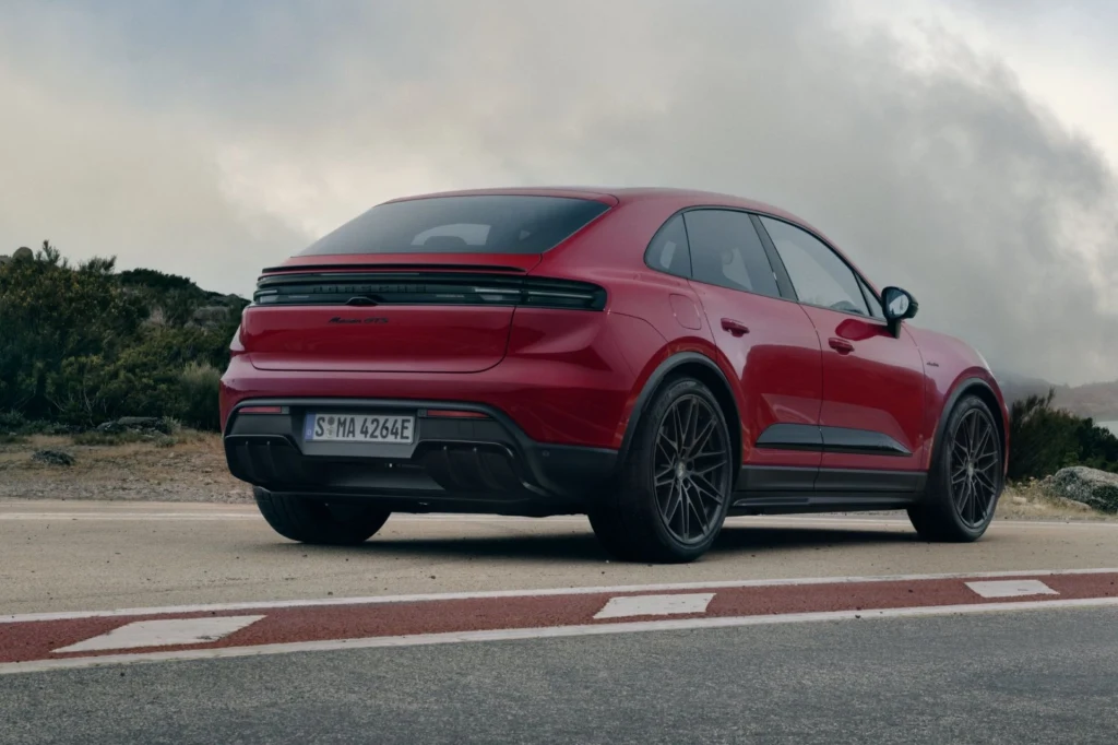 Czerwony sportowy SUV zaparkowany przy drodze, widok z tyłu, dach opadający w stylu coupé, masywne nadkola i eleganckie felgi, w tle niska roślinność i zachmurzone niebo.