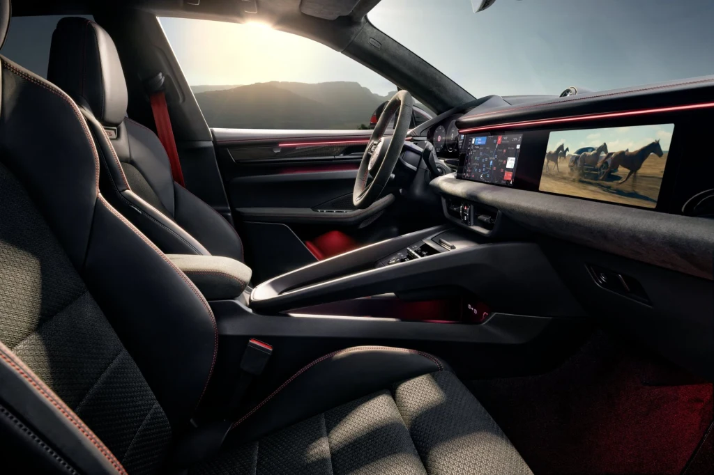 Wnętrze luksusowego samochodu z wysokiej jakości tapicerką, nowoczesną deską rozdzielczą i panoramicznym ekranem wyświetlającym multimedia. Siedzenia wykonane z perforowanej skóry, sportowa kierownica oraz widoczne akcenty w kolorze czerwonym podkreśla...