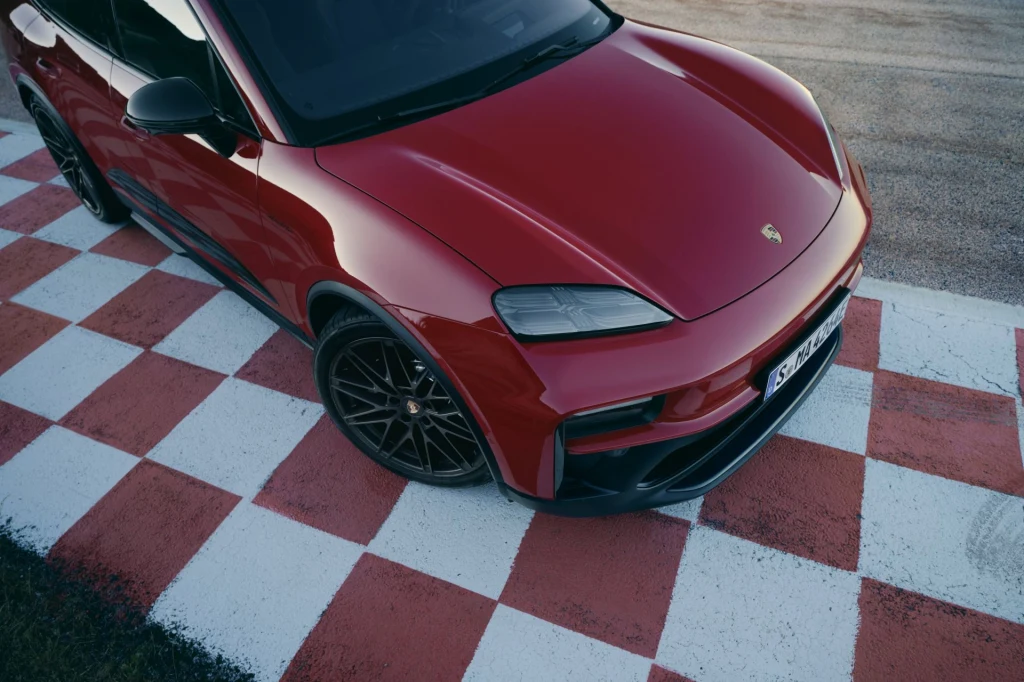 Czerwony samochód Porsche zaparkowany na biało-czerwonych, szachownicowych pasach, ustawiony pod kątem, eksponujący nowoczesny design maski oraz alufelgi.