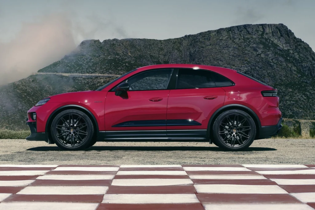 Czerwony samochód sportowy zaparkowany na tle górskiego krajobrazu, widoczny z profilu, asfaltowa nawierzchnia z białymi i czerwonymi pasami na pierwszym planie, w tle szczyt górski i czyste niebo.