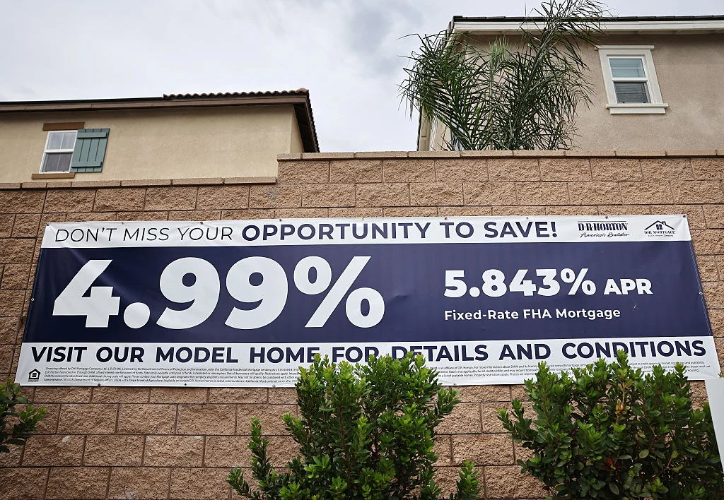 Wiele osób kupuje domy na kredyt Duży szyld promocyjny o stopie procentowej 4,99% oraz 5,843% APR zawieszony na ogrodzeniu z cegły, z fragmentem budynku i zielonymi krzewami na pierwszym planie.