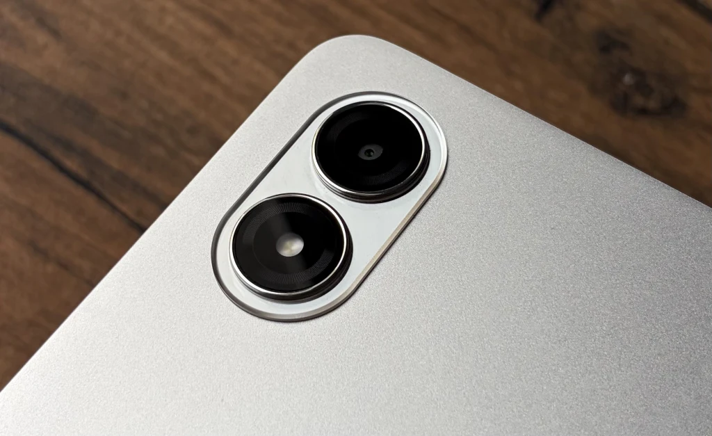 Aparaty fotograficzne Redmi Pad 2 Pro nie są mocną stroną tabletu. Podwójny aparat główny na srebrnej obudowie urządzenia elektronicznego, ukazany na tle drewnianej powierzchni.